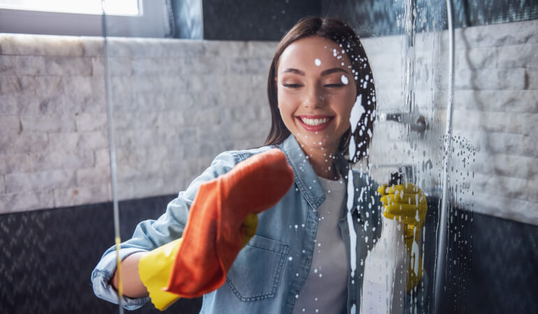 Woman cleaning shower screen in bathroom