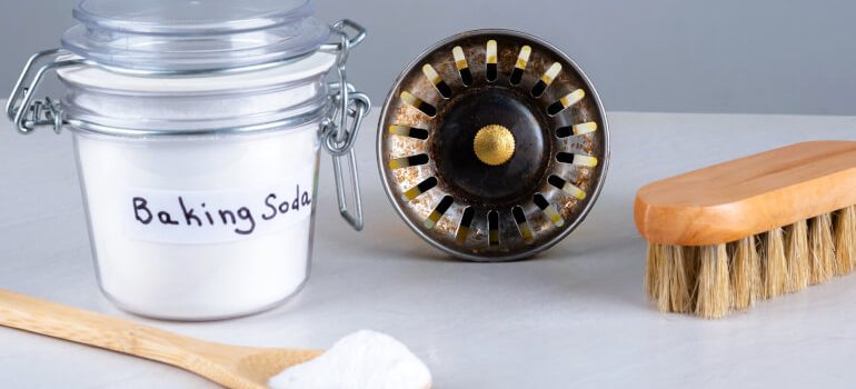 Baking soda, kitchen sink hole and wooden brush, spoon on countertop.