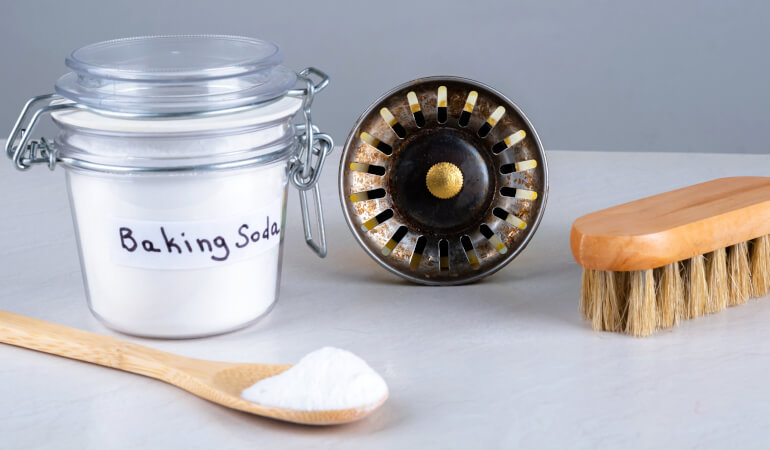 Baking soda, kitchen sink hole and wooden brush, spoon on countertop.