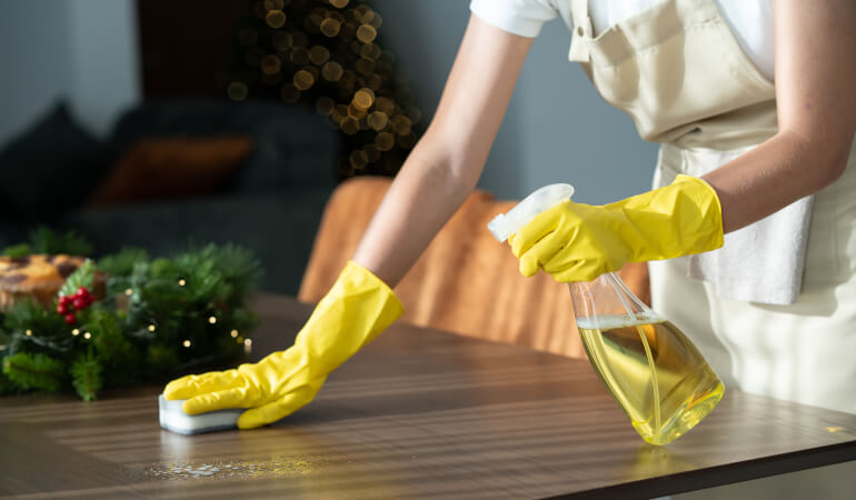Woman cleaning wooden table with homemade Christmas cleaning spray